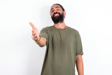 young bearded hispanic man wearing green t-shirt over white background smiling friendly offering handshake as greeting and welcoming. Successful business.