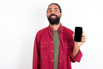 Smiling Caucasian man with beard wearing red shirt over white background Mock up copy space. Hold mobile phone with blank empty screen