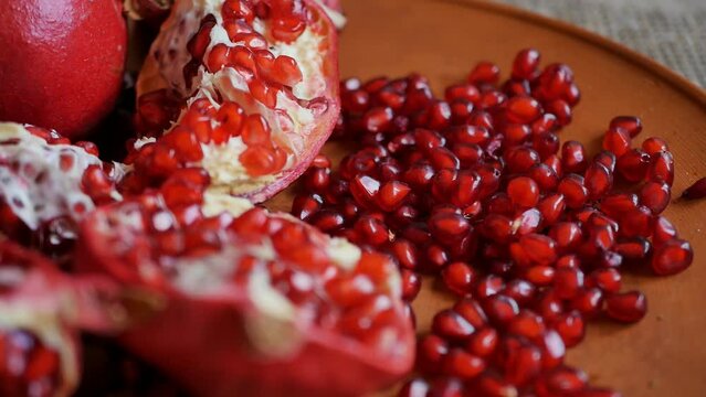 pour red pomegranate seeds into a clay plate with broken pieces of red ripe pomegranates. Close-up. Harvest fresh organic pomegranate