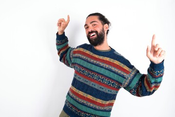 Naklejka premium Photo of upbeat Caucasian man with beard wearing sweater over white background has fun and dances carefree wear being in perfect mood makes movements. Spends free time on disco party