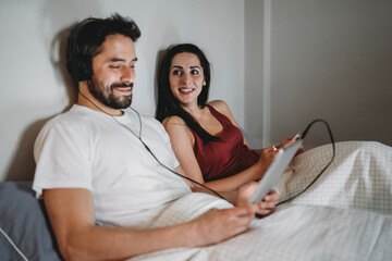 Young couple in bed using the smartphone and the tablet