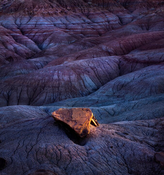 Rare lighting on a solitary rock sitting atop layers of highly erosive soils in Arizona's Painted Desert