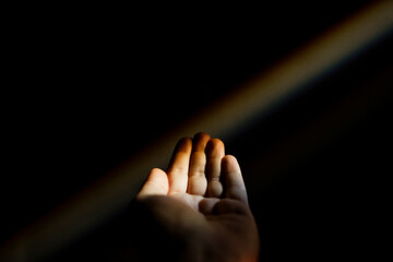 Unrecognizable female hand reaching out to a rainbow in the dark