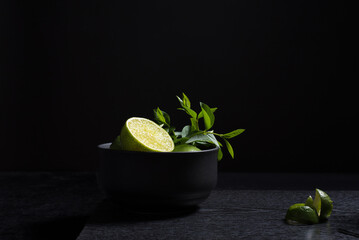 Refrescantes limas verdes en un recipiente negro sobre un fondo oscuro