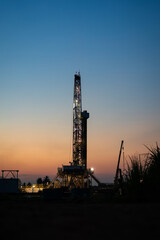 Oil field drilling rig derrick structure on dusk sky background. Industrial and business operation scene. Photo contained noise due to low light environment.