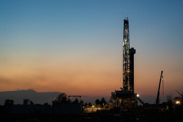 Oil field drilling rig derrick structure on dusk sky background. Industrial and business operation scene. Photo contained noise due to low light environment.