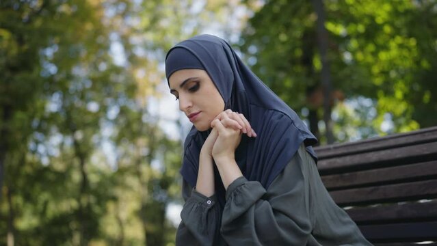 Upset muslim woman sitting on bench in park alone, feeling worried, anxiety