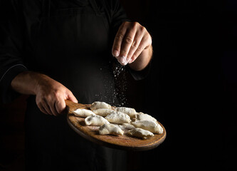 Professional chef throws flour on meat dumplings on a cutting board. Concept for a hotel menu on a black background with space for advertising
