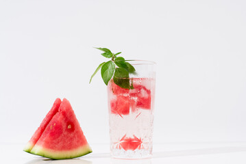 Vaso de zumo de sandía con trozos de sandia y hielo sobre fondo claro	