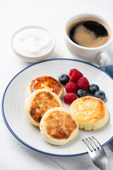 Sweet cottage cheese fritters Syrniki served with berries, cup of black coffee and greek yogurt. Dessert or healthy breakfast food