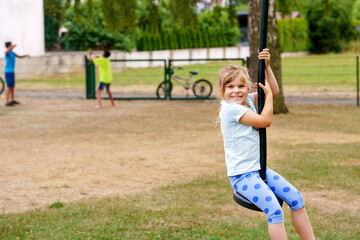 Obraz premium Happy kid girl rids on zip line swing outdoor game play equipment on playground. Child having fun outdoors. Preschool child swinging on summer day. Activity with children.