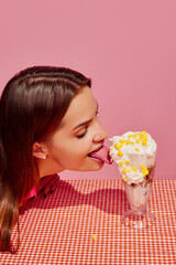 Portrait of young girl eating ice cream cocktail with corn isolated over pink background....