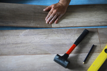 Installing laminated floor, detail on man hands blue wooden tile, over white foam base layer, small pile with more tiles background