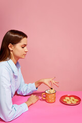 Goodies. Food pop art photography. Young girl tasting milk with crackers isolated over pink background. Concept of food, creativity.