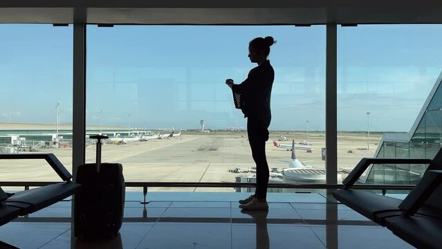 Female Passenger Luggage Airport Runway View Window. Girl waiting alone with luggage in front of the airport runaway window