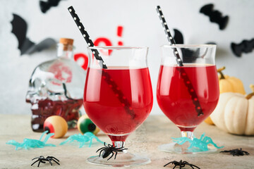 Halloween bloody cocktails. Two bloody cocktails glass goblets for Halloween and bottle form skull on light backgrounds. Decor concept for Halloween party with candy eyes, bats, spiders and pumpkins.