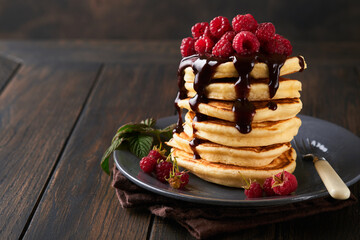Pancakes. Pancakes with fresh raspberry with chocolate glaze or toppings in gray bowl on old wooden table background. Homemade classic american pancakes. Page for magazine concept.