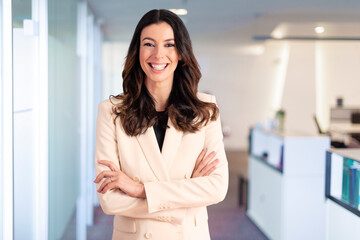 Brunette haired businesswoman looking at camera and smiling while standing at the office