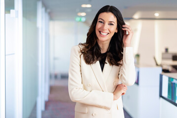 Brunette haired businesswoman looking at camera and smiling while standing at the office