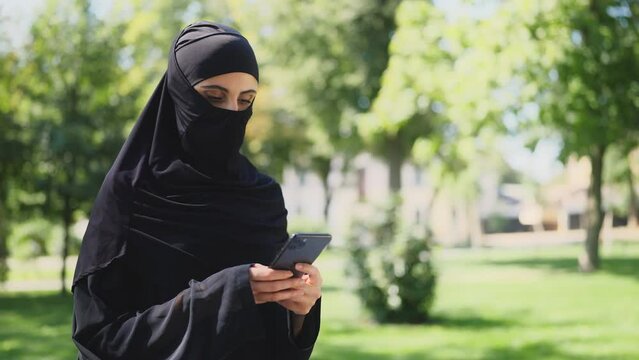 Muslim woman in middle-eastern clothing using smartphone, strict dress code
