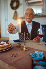 Close up of senior man lighting candles in menorah while celebrating Jewish festival of lights.