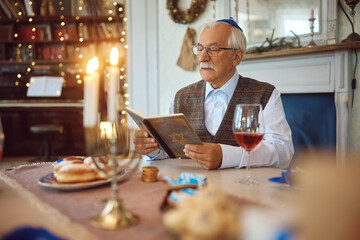 Senior Jewish man reads Tanakh during Hanukkah at home. - obrazy, fototapety, plakaty