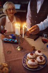 Close up of senior couple lighting candles in menorah during Hanukkah celebration.