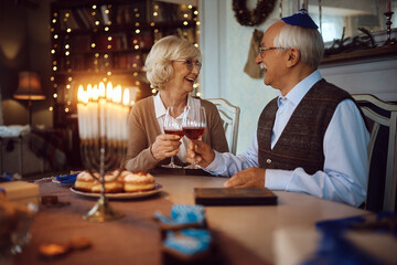 Happy senior couple toasting with wine while celebrating Hanukkah at home.