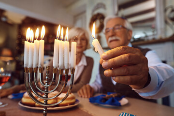 Close up of mature Jew celebrating Hanukkah with his wife and lighting menorah at home.