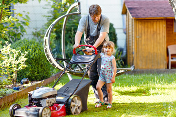 Happy little toddler girl and middle-aged father with lawn mower. Family, daughter, preschool child...
