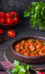 Chashushuli, thick beef stew in tomato sauce with sweet pepper, onion and spices in a clay bowl on a dark wooden background. Beef recipes.