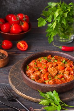 Chashushuli, thick beef stew in tomato sauce with sweet pepper, onion and spices in a clay bowl on a dark wooden background. Beef recipes.
