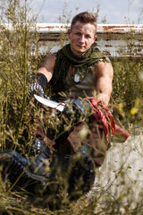 vandal man in dirty clothes sits on an abandoned grassy road, on a bridge