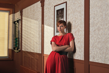 portrait of glamourous woman standing at wall in billiard pool club with hands crossed on chest. woman wearing elegant red dress looking aside