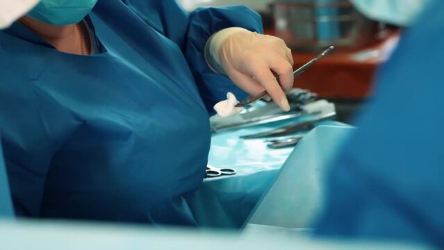 Surgeons in the operating room perform an operation on a patient. A complex surgical operation. The nurse hands the surgeons a scalpel and other surgical items