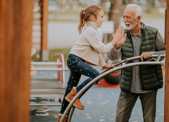 Grandfather spending time with his granddaughter in park playground on autumn day