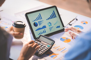 Young colleagues discuss business and analytical price charts using calculators and laptops to calculate financial, tax, accounting, statistics and analytical research ideas.