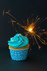 Tasty cupcake with sparkler on wooden table. Cake with blue cream. Photo in low key. Festive dessert and congratulations.