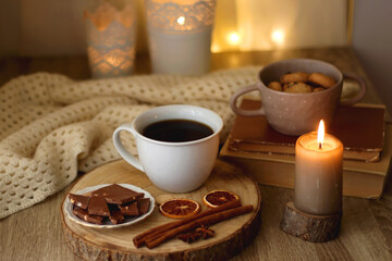 Obraz na płótnie Canvas Bowl of cookies, cup of tea or coffee, chocolate, spices, knitted blanket, books, glasses and candle on the table. Cozy hygge atmosphere at home. Selective focus.