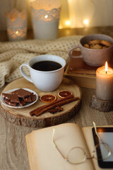 Bowl of cookies, cup of tea or coffee, chocolate, spices, knitted blanket, books, glasses and candle on the table. Cozy hygge atmosphere at home. Selective focus.