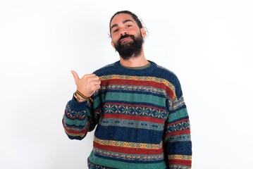 Naklejka premium Caucasian man with beard wearing sweater over white background points away and gives advice demonstrates advertisement
