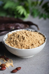 Carob pods and carob powder over a stone background.
