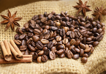 Coffee beans of medium roast Arabica coffee beans, anise stars and cinnamon sticks on sackcloth. Flavoured toning coffee drink. Beans closeup, coffee beans background. Espresso aroma, caffeine drink
