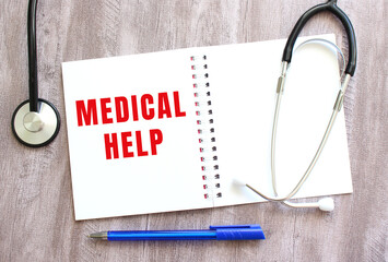 White notebook with red text MEDICAL HELP and a stethoscope on a gray wooden table.