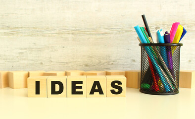 Five stacked wooden cubes with letters IDEAS on a white desktop on a gray background.