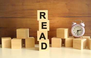 Four wooden cubes stacked vertically on a brown background form the word READ.