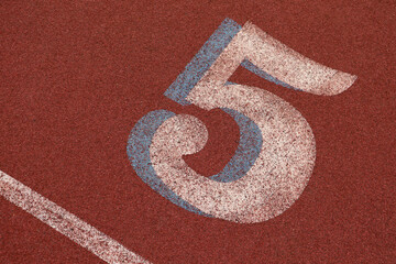 Fifth lane on an athletics track showing a number five on a red athletics track