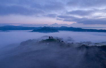Cerkev Sveti Tomaž (St. Thomas Church) near Škofja Loka, Slovenia. Foggy morning and sunrise, drone photo