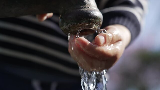 Closeup of flowing water faucet child hand and mouth drinking outdoors at public park. One little boy hydrating himself