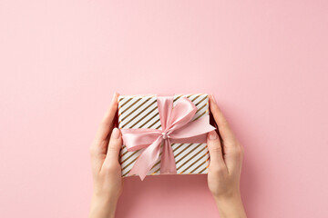New Year celebration concept. First person top view photo of young woman's hands giving big present box with pink ribbon bow on isolated pastel pink background with copyspace